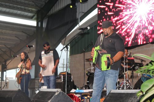 A band performs on stage with an accordion player, a washboard player, and a guitarist, surrounded by musical equipment.