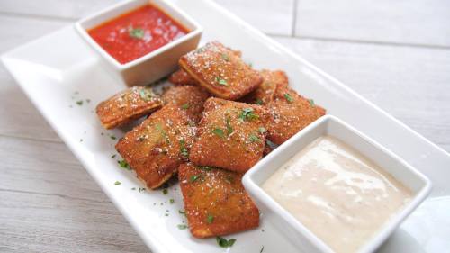 A plate of golden-brown fried snacks served with marinara and creamy dipping sauces, garnished with herbs.