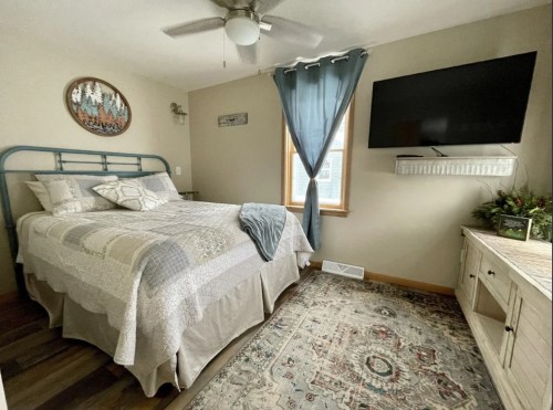 Cozy bedroom featuring a blue metal bed, patterned bedding, a TV on the wall, and a decorative rug.