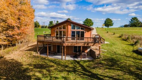 A spacious wooden cabin with large windows, surrounded by trees and a grassy landscape under a blue sky.