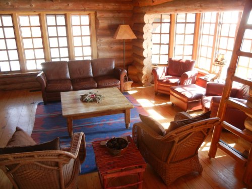 Cozy log cabin living room with leather sofas, wooden furniture, and large windows letting in natural light.