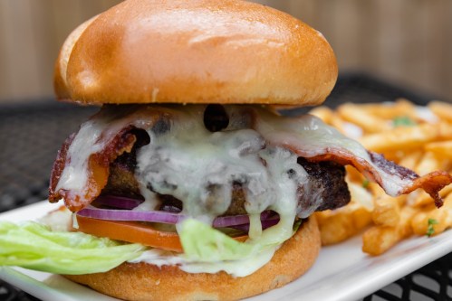 A juicy burger with melted cheese, bacon, lettuce, and tomato, served with a side of crispy fries on a plate.