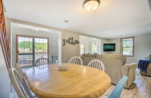 Cozy living space with a round wooden dining table, comfortable seating, and large windows overlooking a lake.