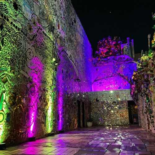 Colorful, illuminated mosaic walls in a vibrant outdoor space at night, featuring intricate designs and patterns.