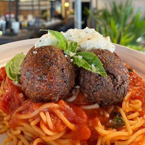 A plate of spaghetti topped with two meatballs, marinara sauce, fresh basil, and a dollop of ricotta cheese.
