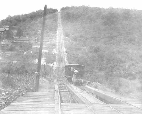 A vintage black-and-white photo of a steep railway incline with a small train ascending a hill.