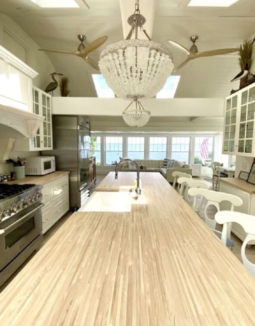 Bright, modern kitchen with a large wooden island, stainless steel appliances, and elegant chandeliers.