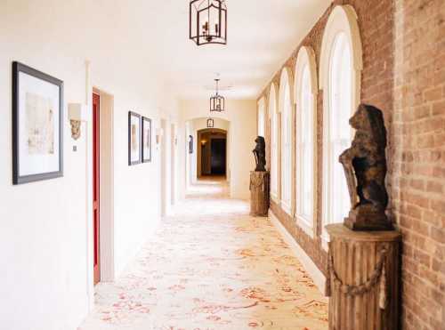 A well-lit hallway with arched windows, artwork on the walls, and decorative lion statues on pedestals.