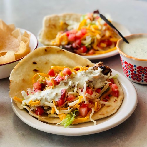 A plate with a taco filled with lettuce, tomatoes, cheese, and sauce, alongside tortilla chips and a bowl of green sauce.