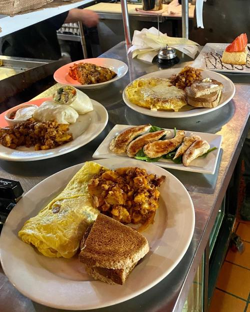 A table with various breakfast dishes, including an omelet, toast, chicken, and sides, in a diner setting.