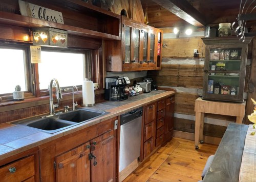 Cozy kitchen with wooden cabinets, a double sink, coffee maker, and a vintage cabinet against a rustic wall.