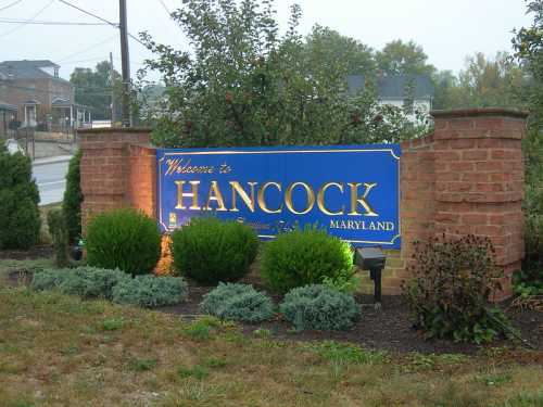 Welcome sign for Hancock, Maryland, surrounded by greenery and brick landscaping on a foggy day.