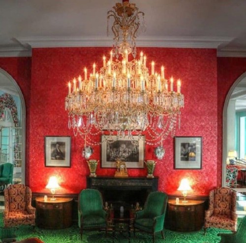 Luxurious room with a grand chandelier, red wallpaper, and elegant furniture, creating an opulent atmosphere.