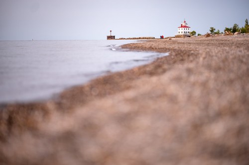 A serene beach scene with a lighthouse in the distance and gentle waves lapping at the shore.