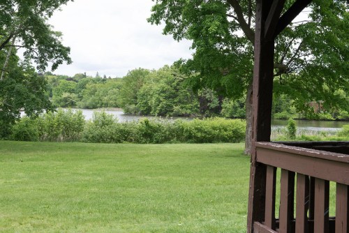 A serene view of a lake surrounded by lush greenery, seen from a wooden gazebo.