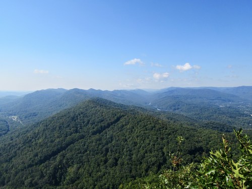 A panoramic view of lush green mountains under a clear blue sky, with a river winding through the valley below.