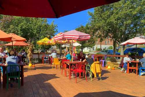 Outdoor dining area with colorful chairs and umbrellas, featuring patrons enjoying a sunny day surrounded by autumn decor.