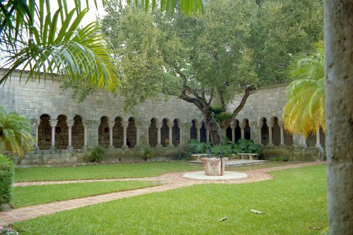 A serene courtyard with stone arches, lush greenery, and a large tree in the center, creating a peaceful atmosphere.