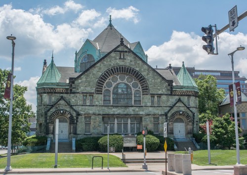 Historic stone building with green copper accents, large arched windows, and a decorative roof under a blue sky.