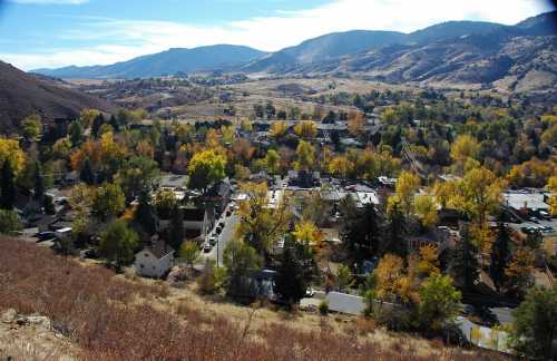 Aerial view of a small town surrounded by mountains and colorful autumn trees under a clear blue sky.