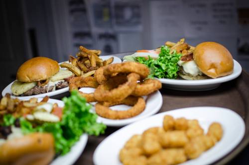 A variety of burgers with toppings, onion rings, fries, and tater tots on plates, arranged appetizingly.