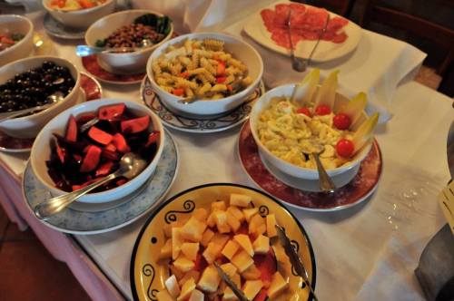 A variety of dishes including pasta salad, fruit, olives, and sliced meats arranged on a table.