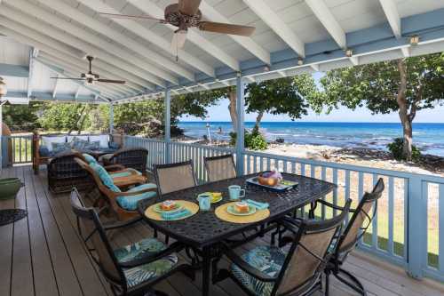 A spacious porch with a dining table, chairs, and ocean views, surrounded by greenery and a relaxing atmosphere.