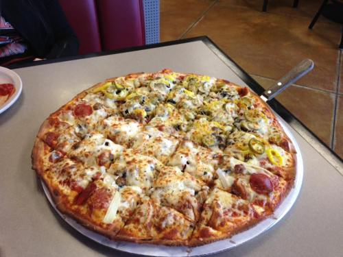 A large pizza on a table, topped with pepperoni, olives, green peppers, and cheese, cut into slices.