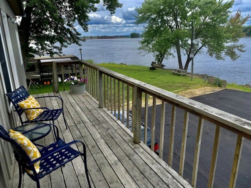 A wooden deck with two chairs and a cushion overlooks a river and trees under a cloudy sky.