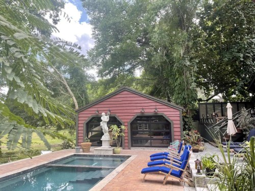 A cozy backyard with a pool, a red shed, and lounge chairs surrounded by lush greenery and trees.