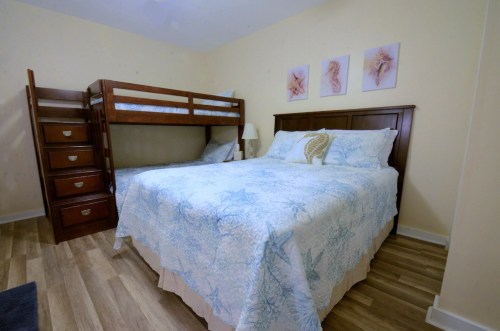 A cozy bedroom featuring a double bed and a bunk bed, with light-colored walls and beach-themed decor.