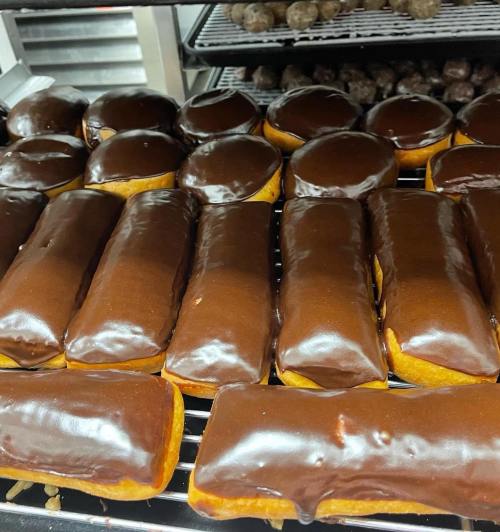 A tray of freshly glazed chocolate donuts, including round and rectangular shapes, cooling on a wire rack.