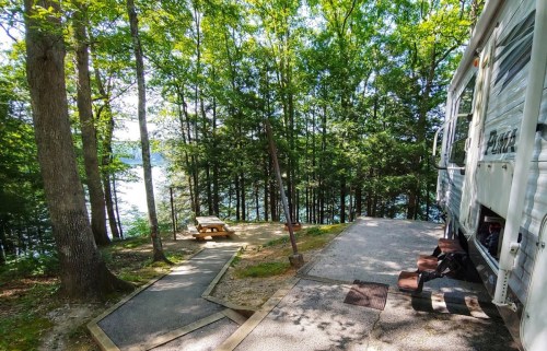 A serene campsite by a lake, surrounded by trees, featuring a picnic table and a parked RV.