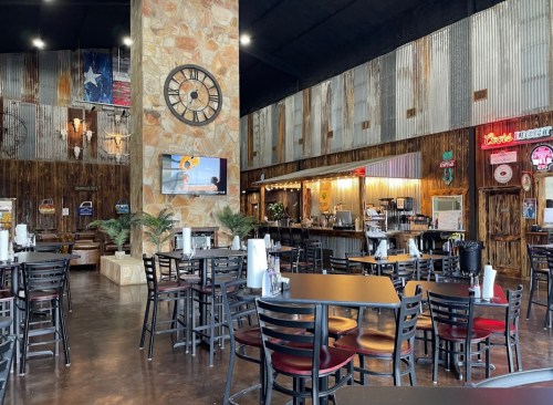 Interior of a rustic restaurant with wooden decor, tables, a bar area, and a large clock on the wall.