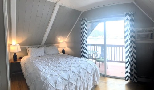 Cozy bedroom with a white bedspread, two lamps, and large windows leading to a balcony.