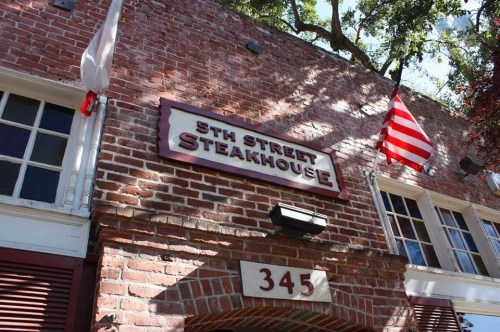 Sign for "5th Street Steakhouse" on a brick building, with American flags and a street number visible.