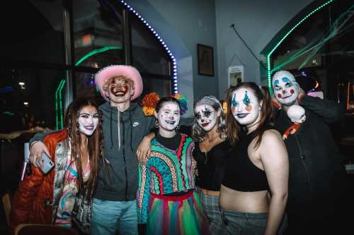 A group of six people in colorful costumes and clown makeup, posing together in a festive setting.