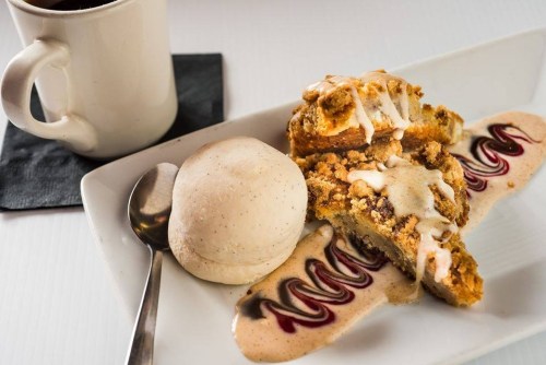 A slice of dessert with a scoop of ice cream, drizzled with sauce, served on a plate alongside a cup of coffee.