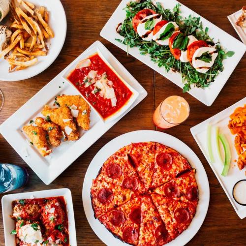 A spread of delicious dishes including pizza, salad, fries, and chicken, arranged on a wooden table.
