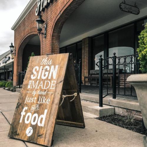 A wooden sign outside a restaurant reads, "This sign was made by hand, just like our food."