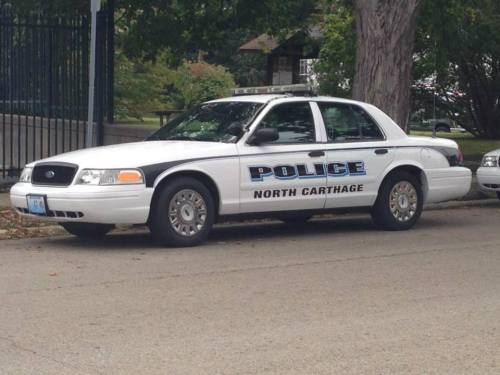 A white police car parked on a street, marked with "POLICE" and "NORTH CARTHAGE" on the side.
