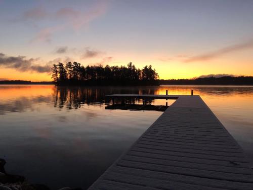 A serene sunset over a calm lake, with a wooden dock extending into the water and silhouettes of trees in the background.