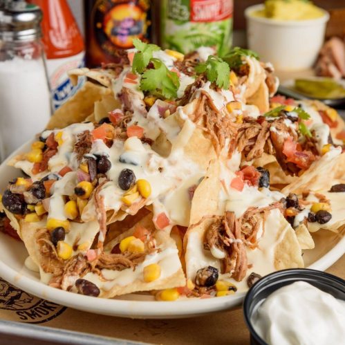 A plate of loaded nachos topped with pulled pork, cheese, black beans, corn, tomatoes, and fresh cilantro.