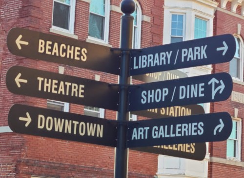 A directional signpost with arrows pointing to various locations: Beaches, Library/Park, Theatre, Shop/Dine, Downtown, Art Galleries.