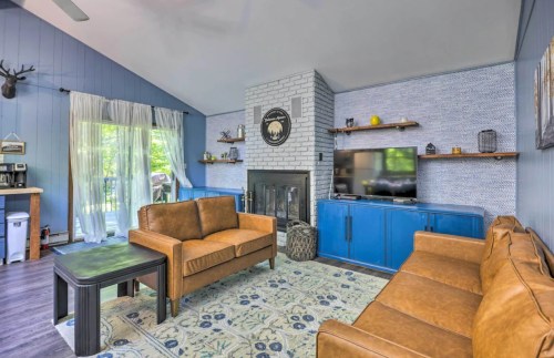 Cozy living room with blue walls, a fireplace, two brown sofas, a TV, and large windows letting in natural light.