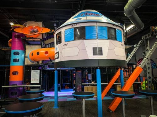 A colorful indoor play area featuring a spaceship-themed structure and various climbing equipment.