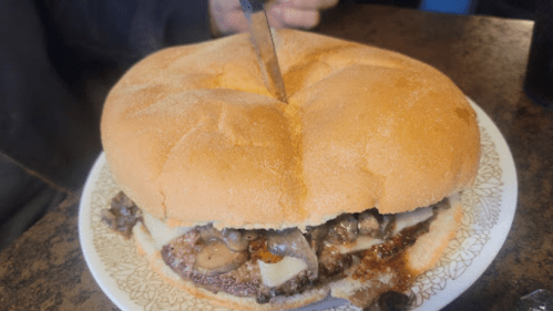 A large sandwich with mushrooms and cheese, topped with a knife, on a plate at a restaurant.