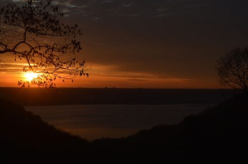 A serene sunset over a calm lake, framed by silhouetted trees against a colorful sky.