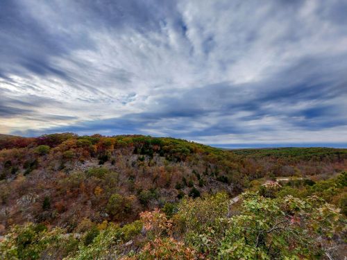 A panoramic view of a colorful autumn landscape with rolling hills under a cloudy sky.