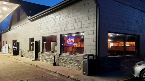A gray building with large windows, featuring an illuminated "OPEN" sign, and a clean exterior.